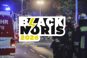 Schriftzug „BLACK NORIS 2026“ mit Blitzsymbol vor einem nächtlichen Feuerwehreinsatz. Im Hintergrund sind Einsatzfahrzeuge, Blaulicht und Feuerwehrkräfte auf einer Straße zu sehen.