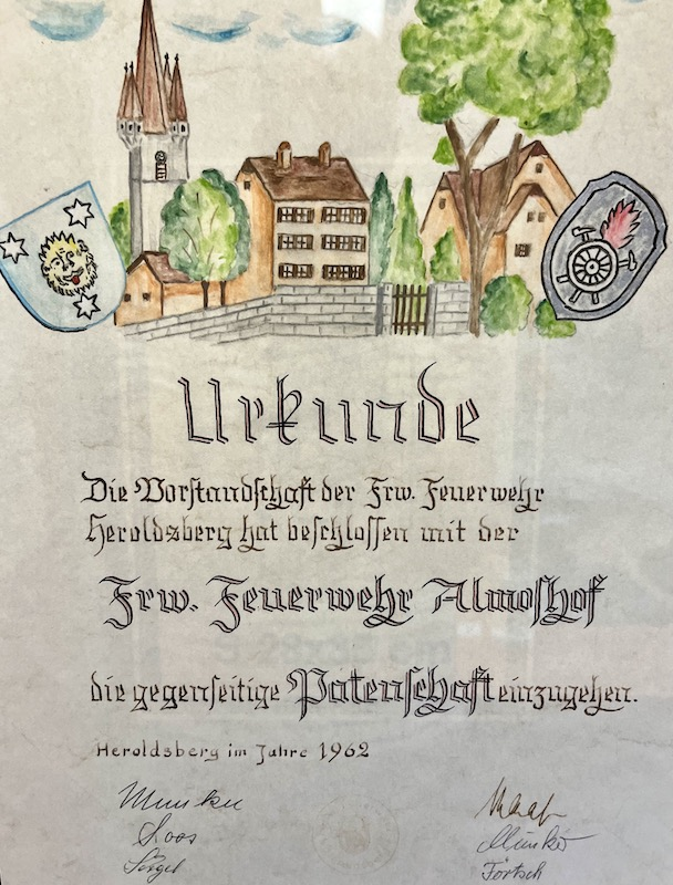 Handgemalte Urkunde aus dem Jahr 1962 zur gegenseitigen Patenschaft zwischen der Freiwilligen Feuerwehr Heroldsberg und der Freiwilligen Feuerwehr Almoshof. Mit farbiger Illustration und Unterschriften.